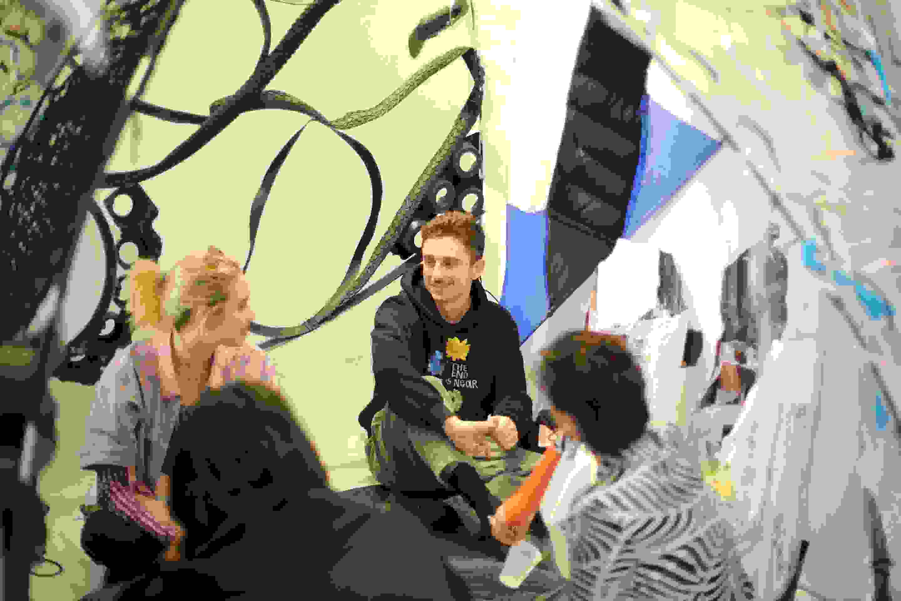 Four people sitting cross-legged on the floor inside of a sculpture and chatting.