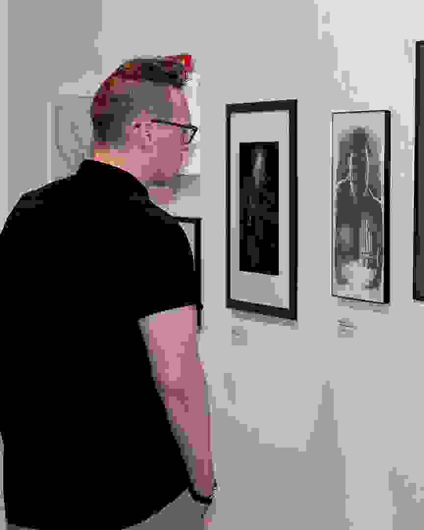 A man stands in front of a gallery wall, staring at a black and white piece.