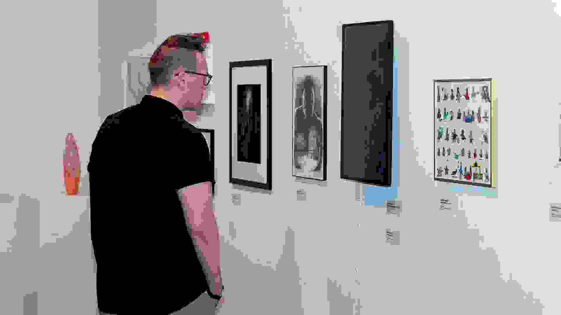 A man stands in front of a gallery wall, staring at a black and white piece.