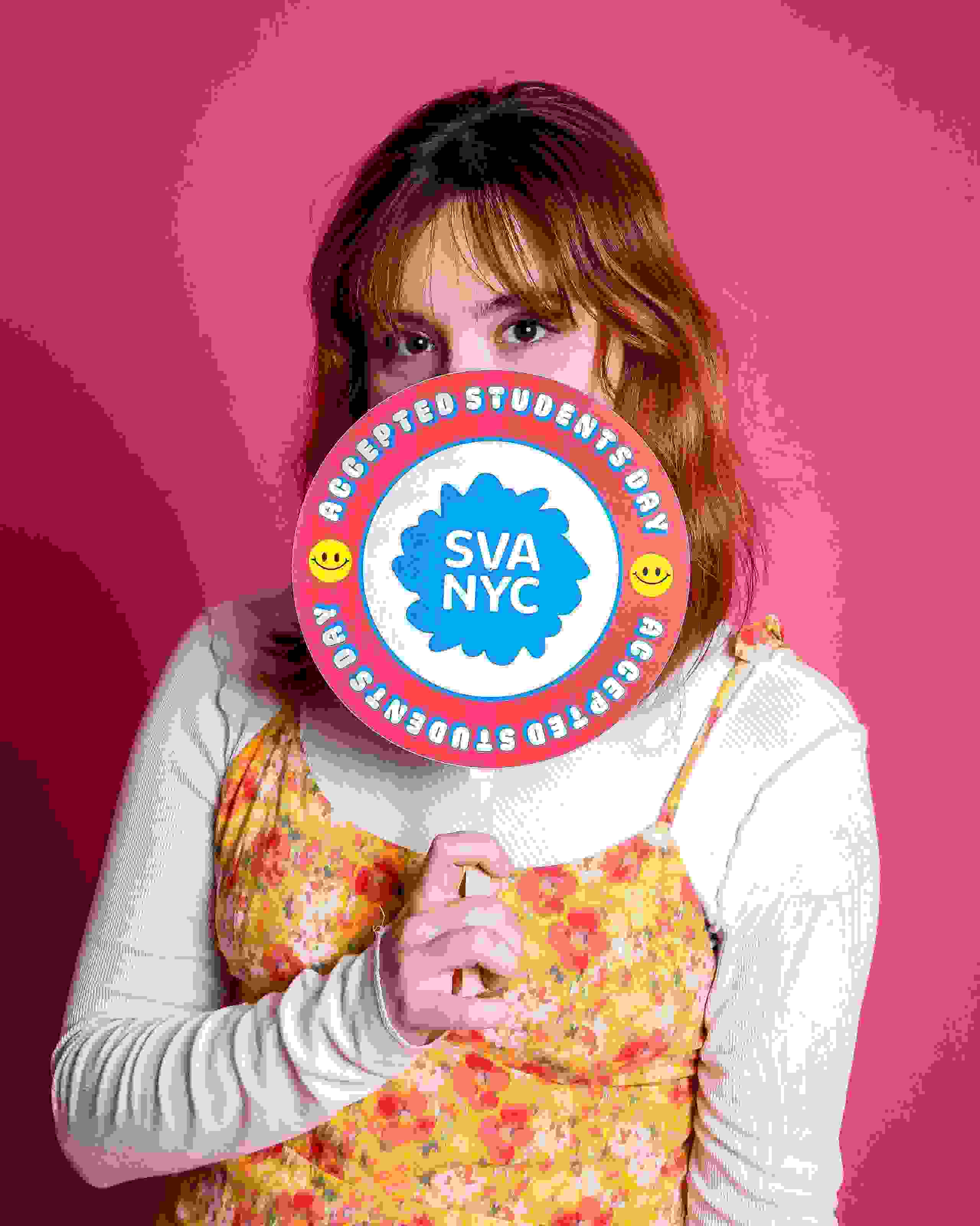 A person poses with a sign reading SVA NYC Accepted Students Day in front of a pink background