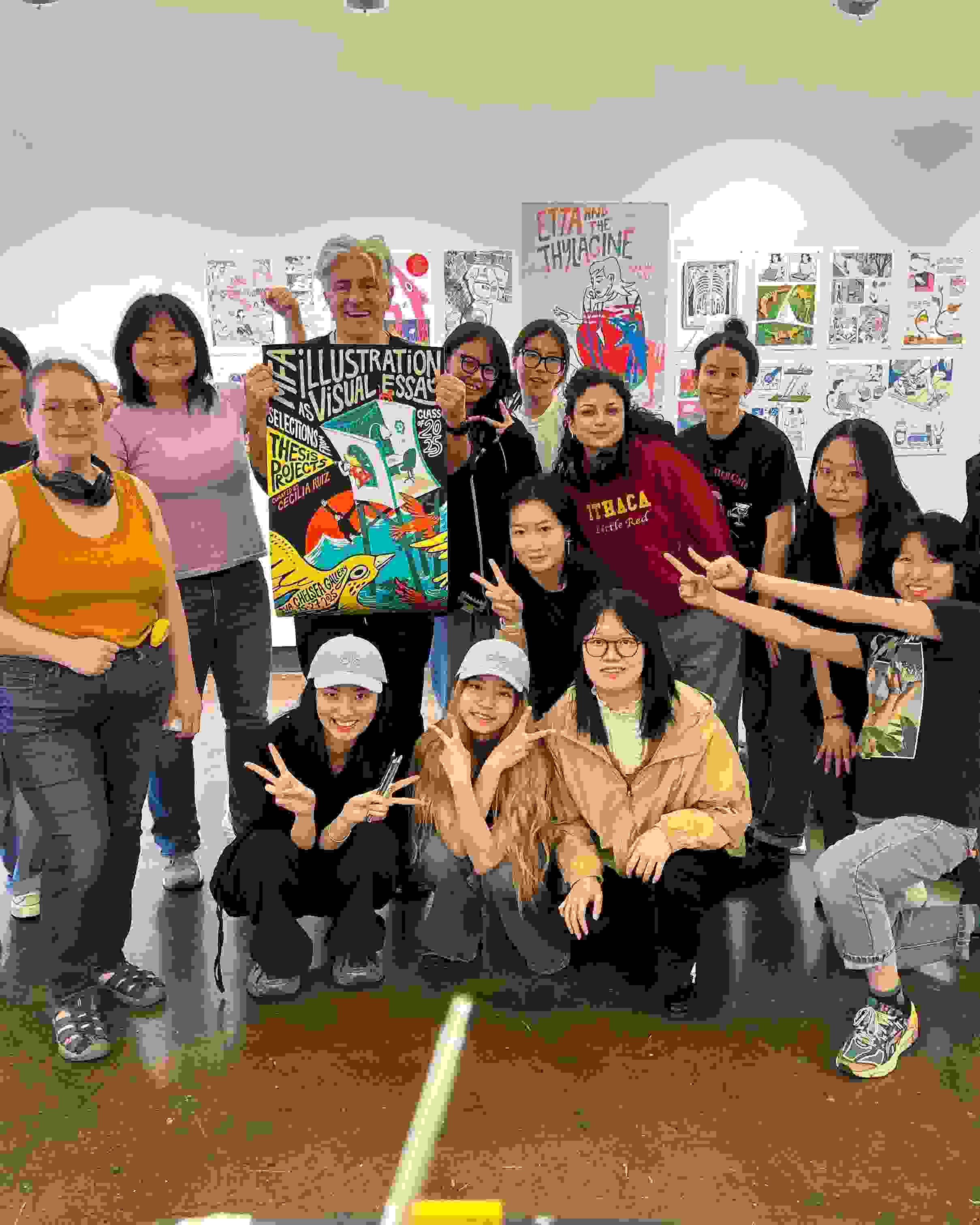 Students pose for a picture in a gallery with an instructor, who is showing off a poster design that they may have all worked on.