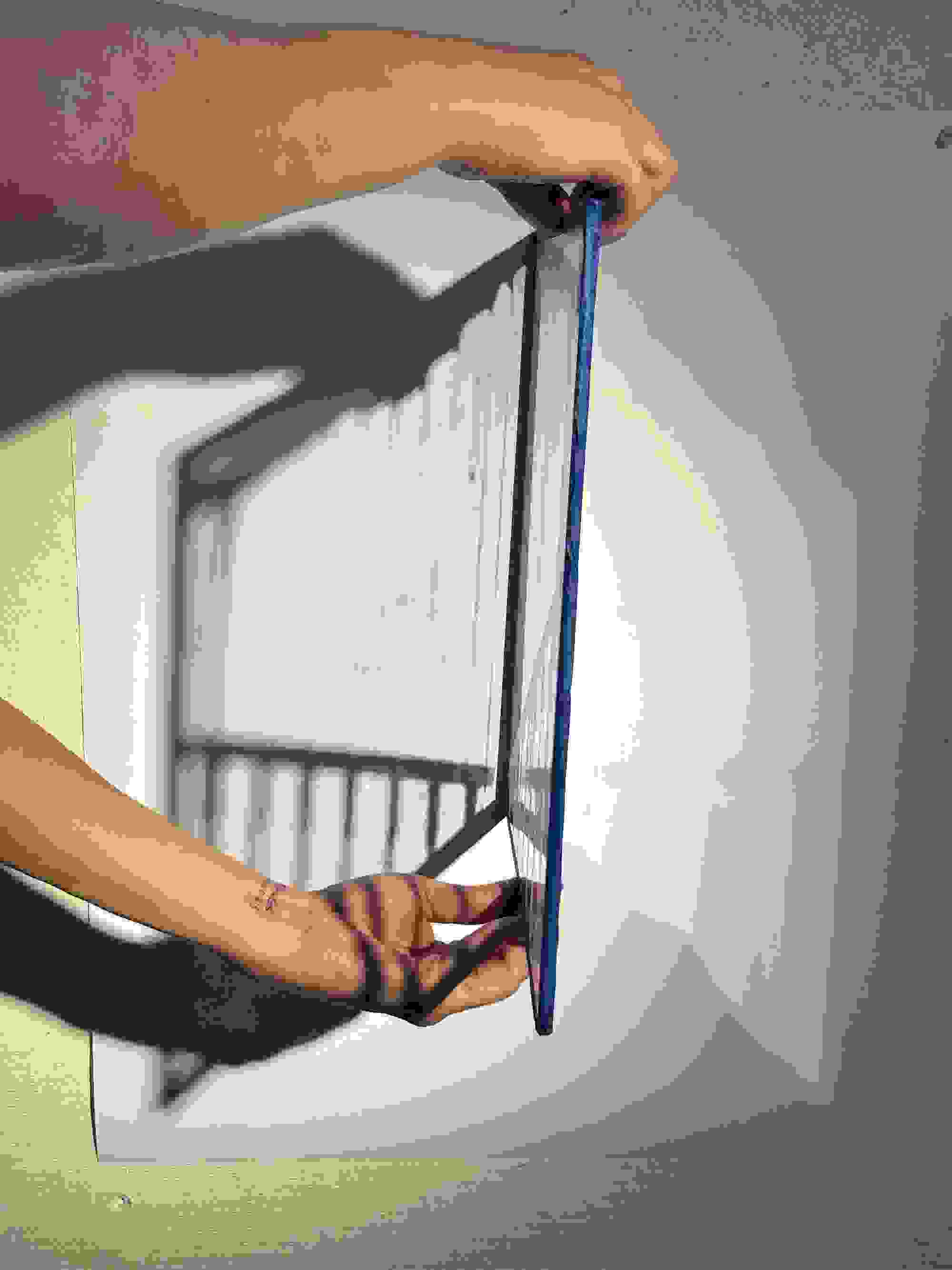 Hands hold a transparent, blue-edged panel casting a lined shadow on a white surface. The scene is minimalistic and abstract.