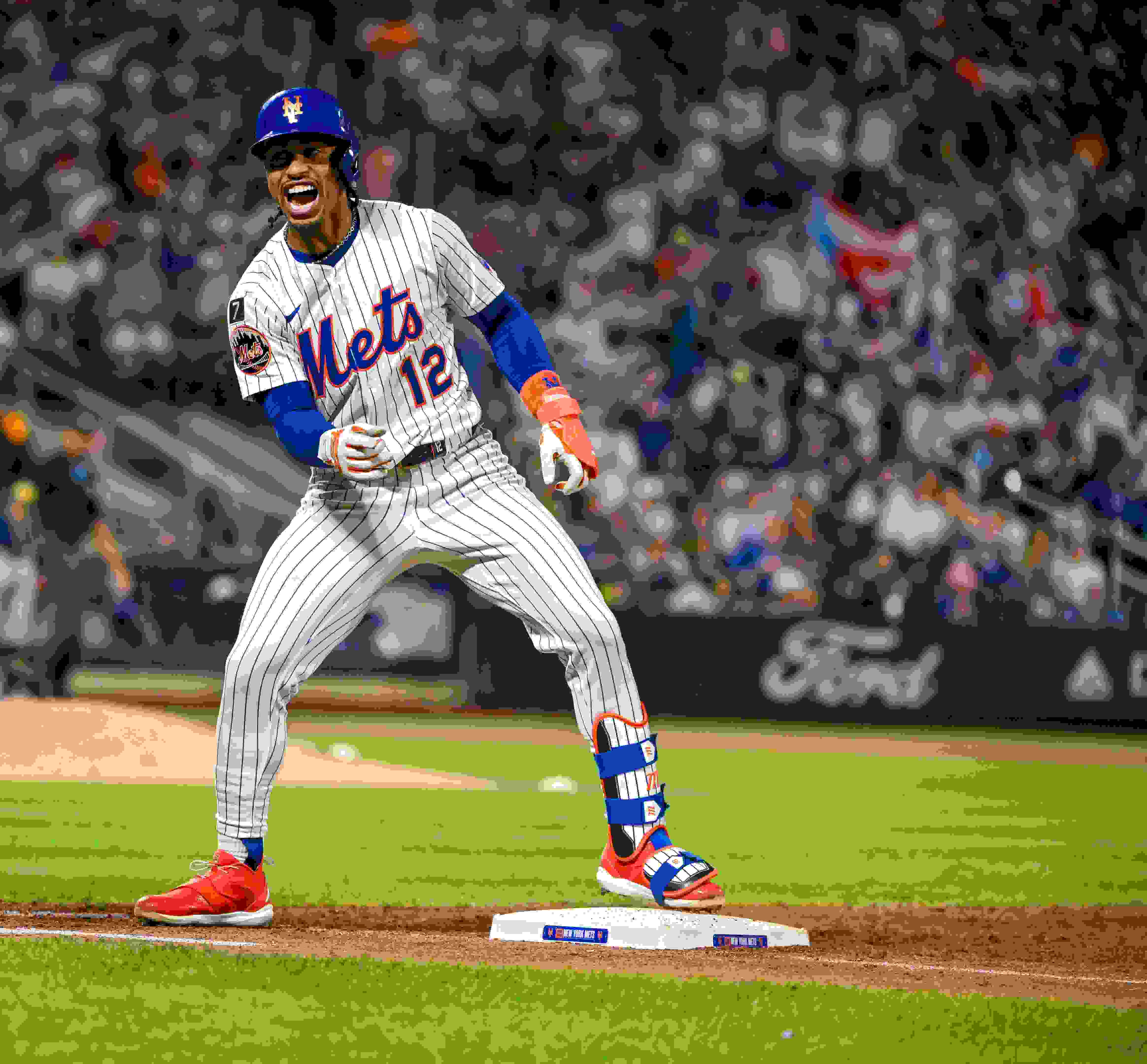 Mets shortstop Francisco Lindor celebrates safely reaching first base. In the crowd in the background, a Puerto Rican flag can be seen.