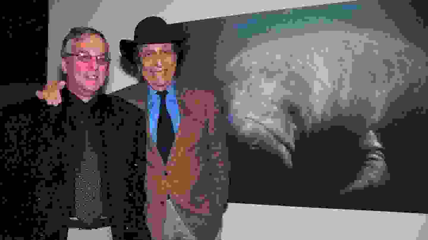 Two people in business casual attire pose for a picture in front of a wall-mounted photograph of a manatee