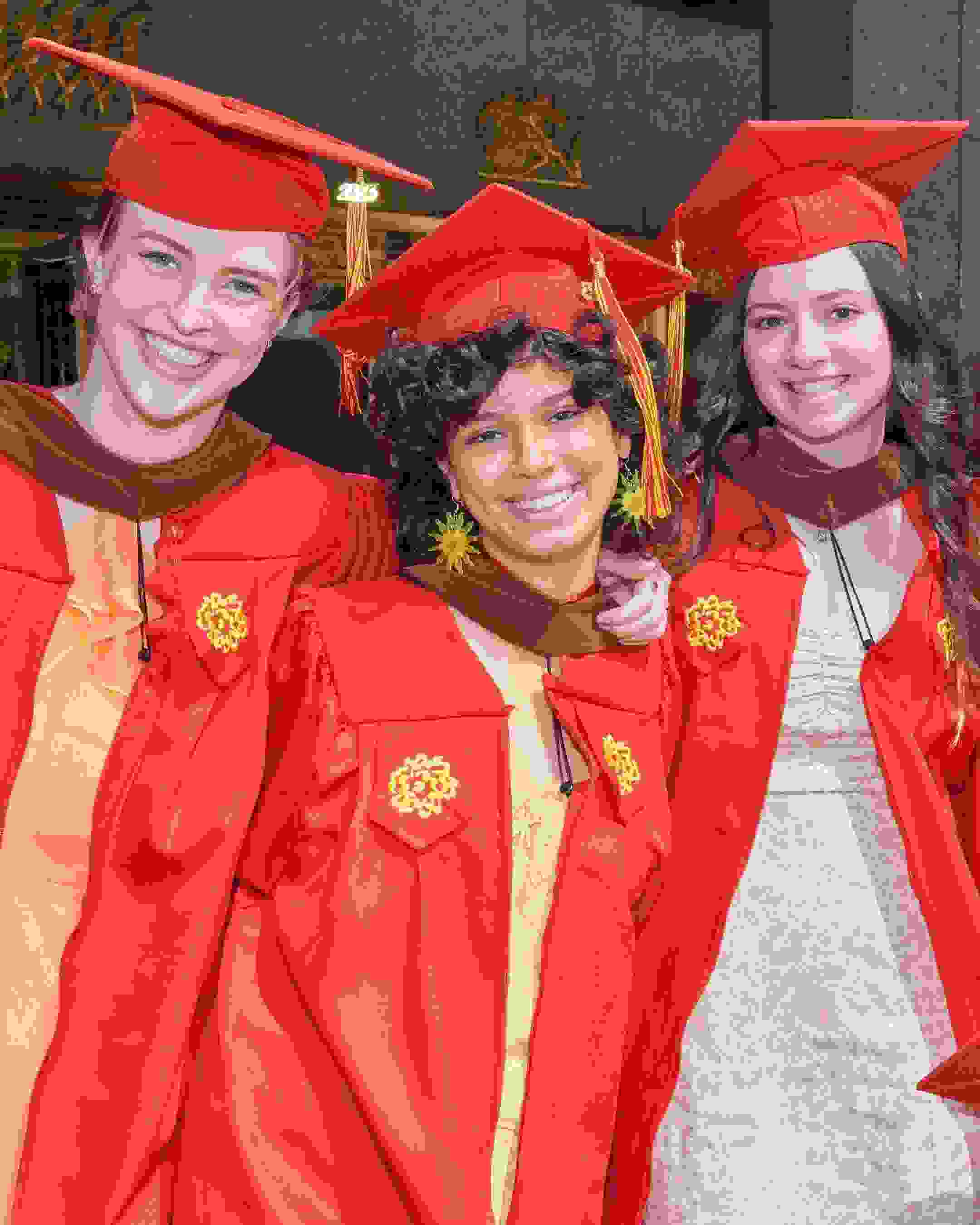 Four members of SVA's class of 2023 pose in red graduation caps and gowns outside of Radio City Music Hall