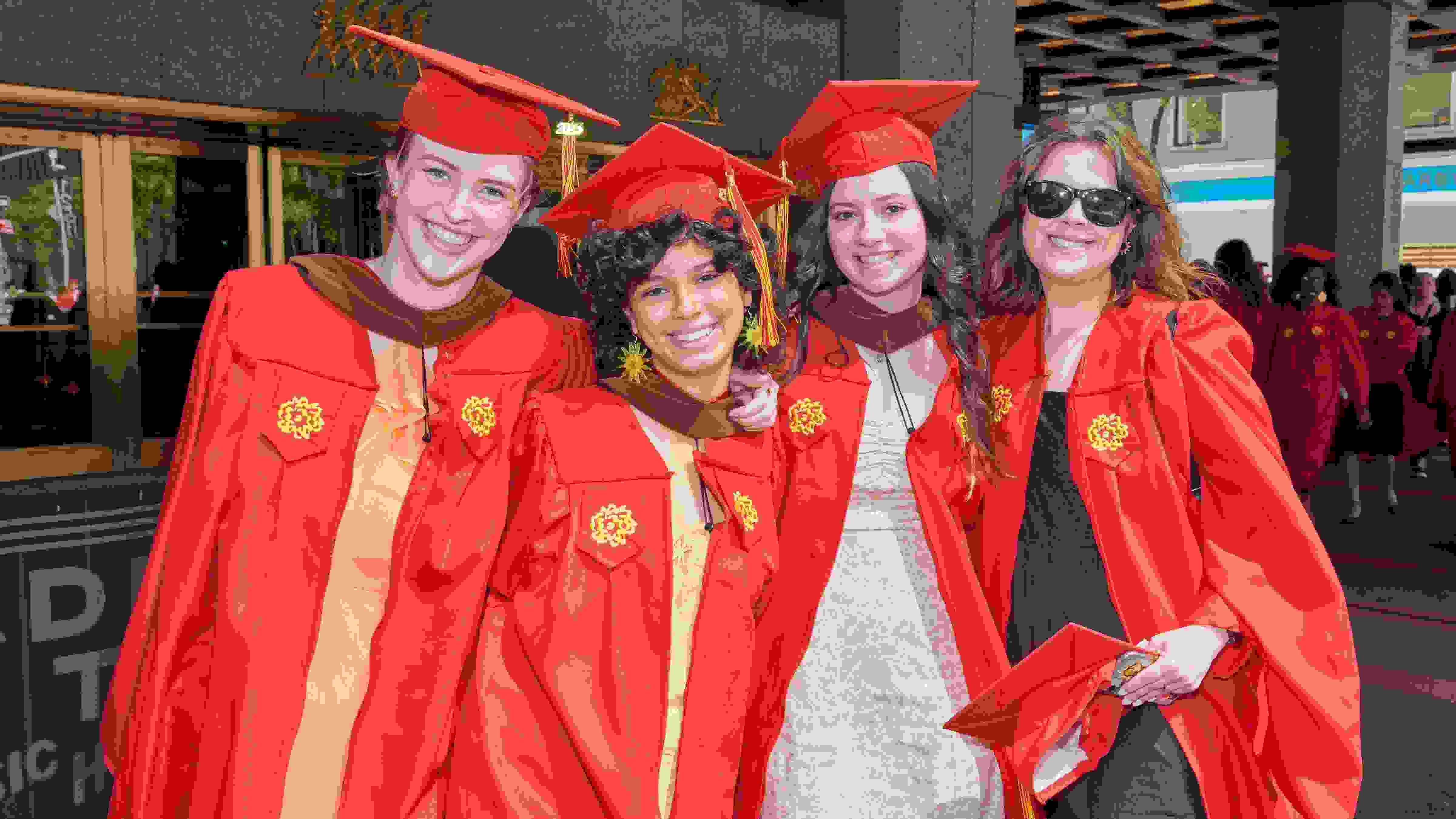 Four members of SVA's class of 2023 pose in red graduation caps and gowns outside of Radio City Music Hall