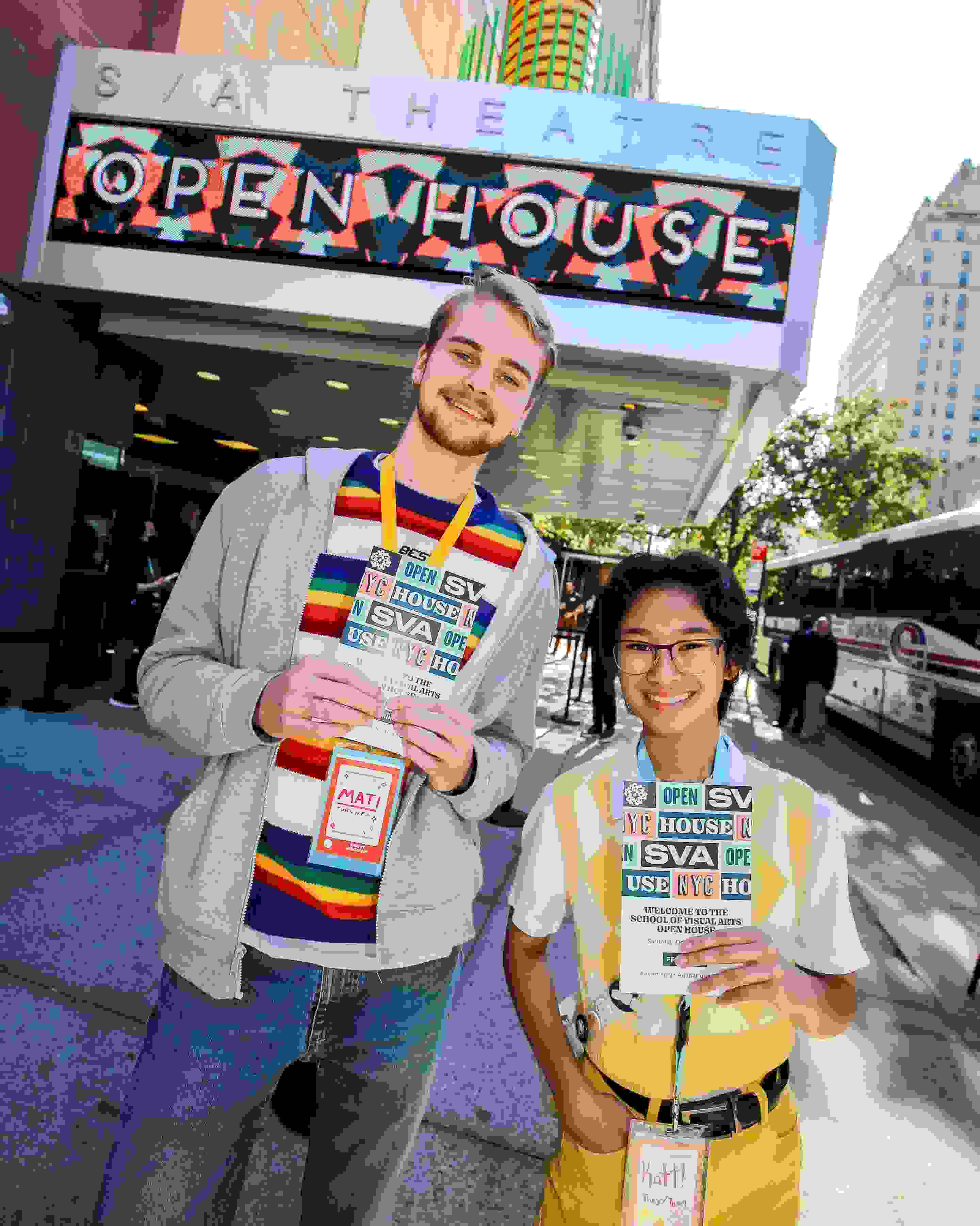 Two student ambassadors wearing bright colors stand in front of a theater