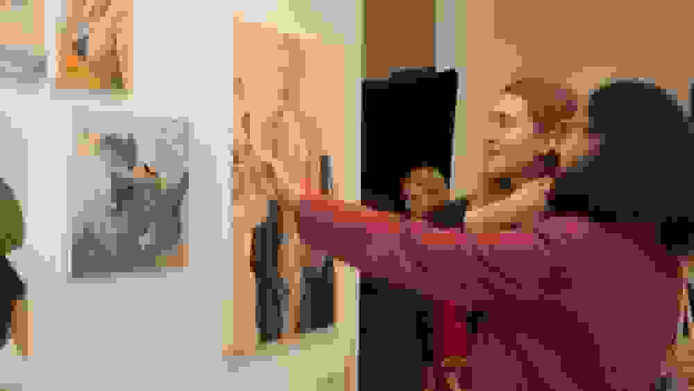 Two students engaging with art mounted on a wall at an exhibition.