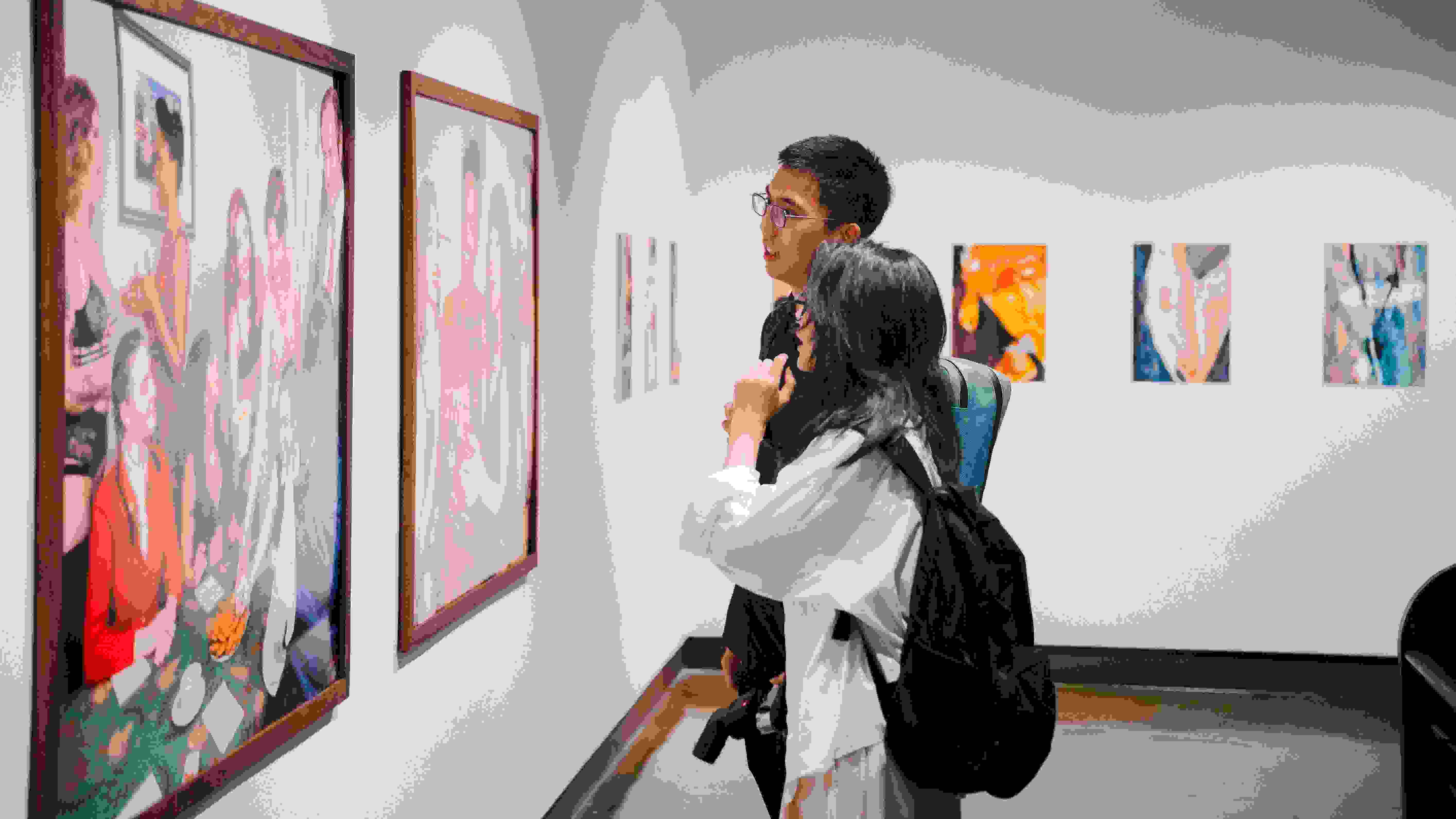 An image of two people standing in front of a gallery wall looking at a photograph.