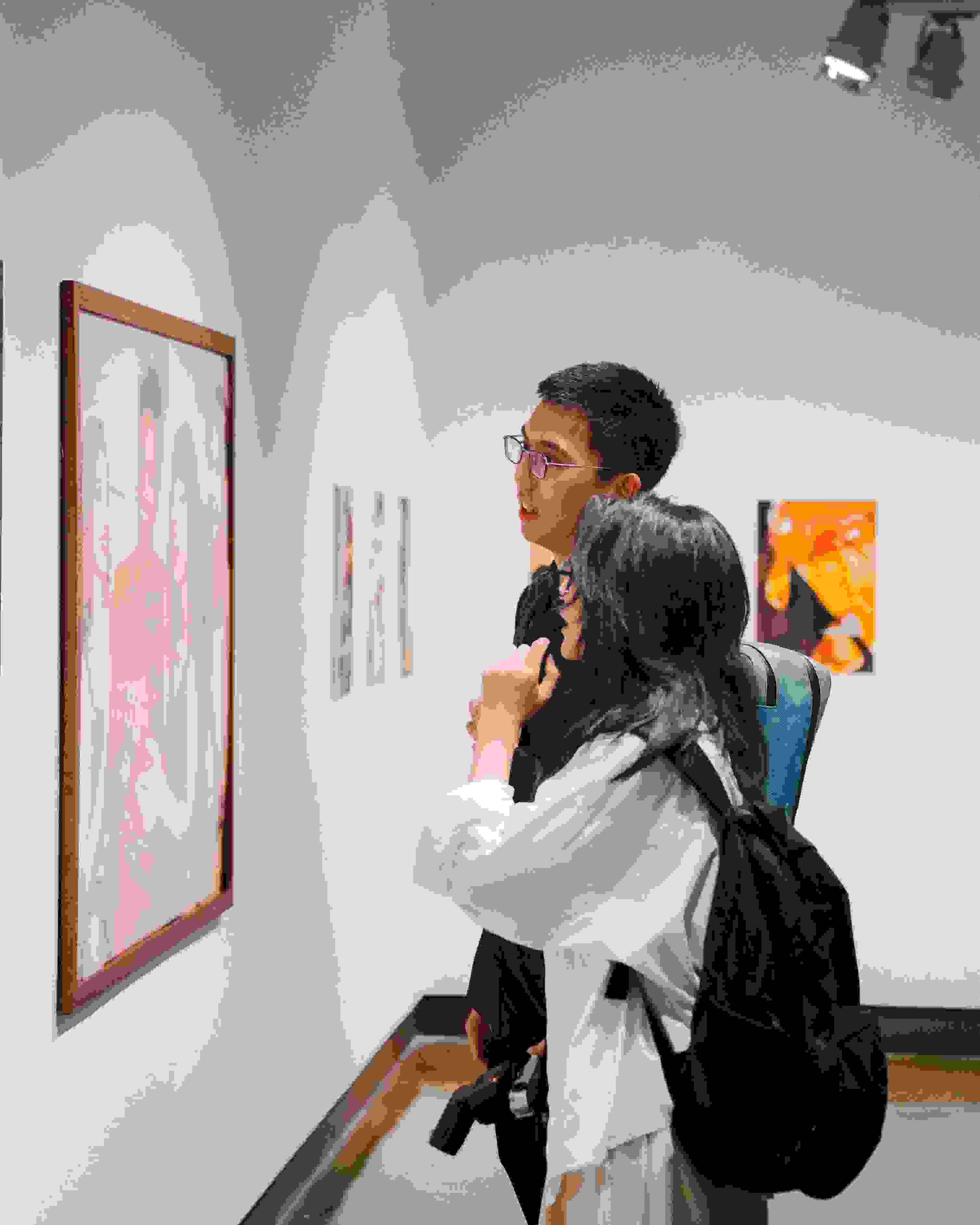 An image of two people standing in front of a gallery wall looking at a photograph.