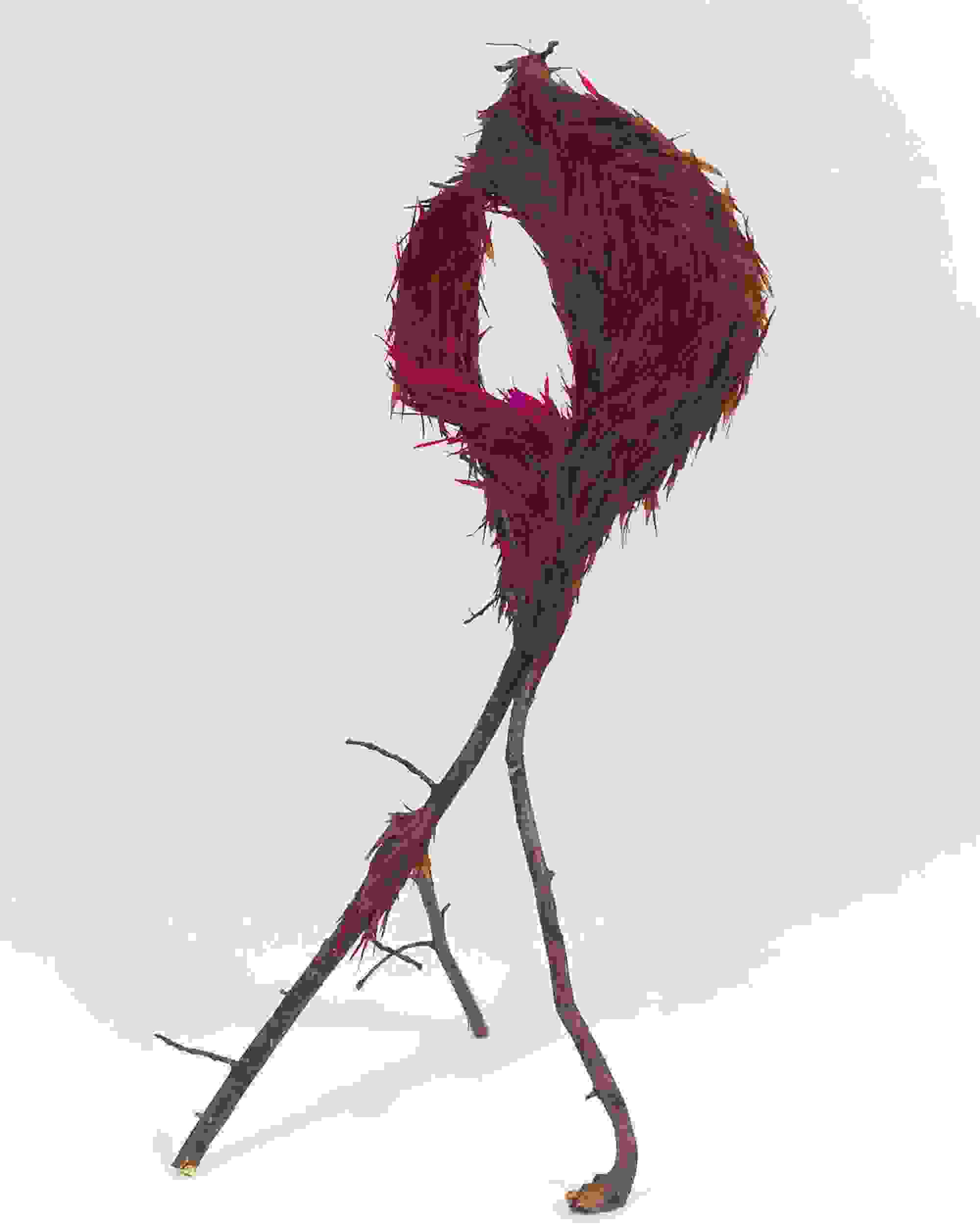 A whimsical sculpture of branches forms a loop at the top, adorned with vibrant magenta and brown feathers, set against a plain white background.
