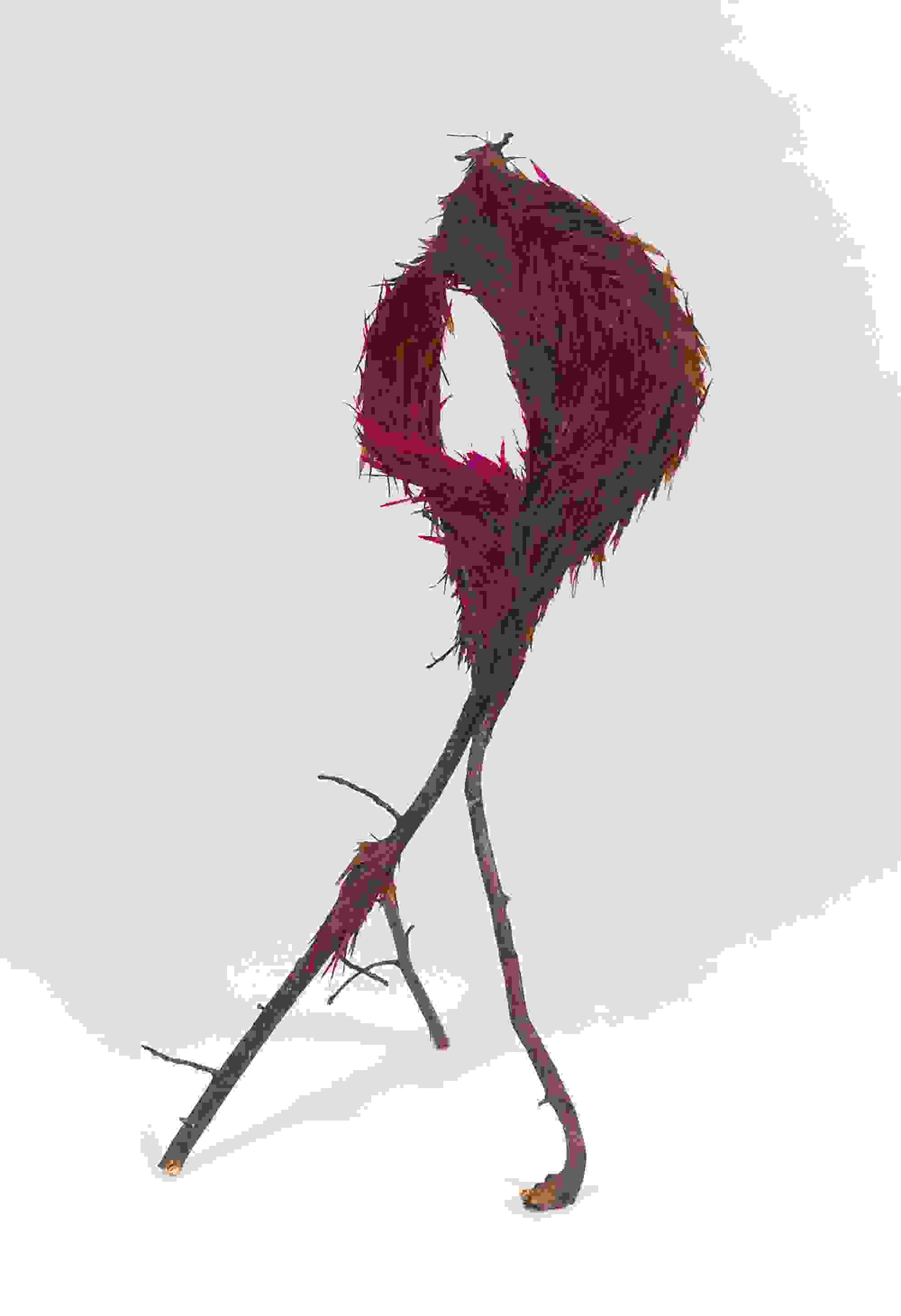 A whimsical sculpture of branches forms a loop at the top, adorned with vibrant magenta and brown feathers, set against a plain white background.