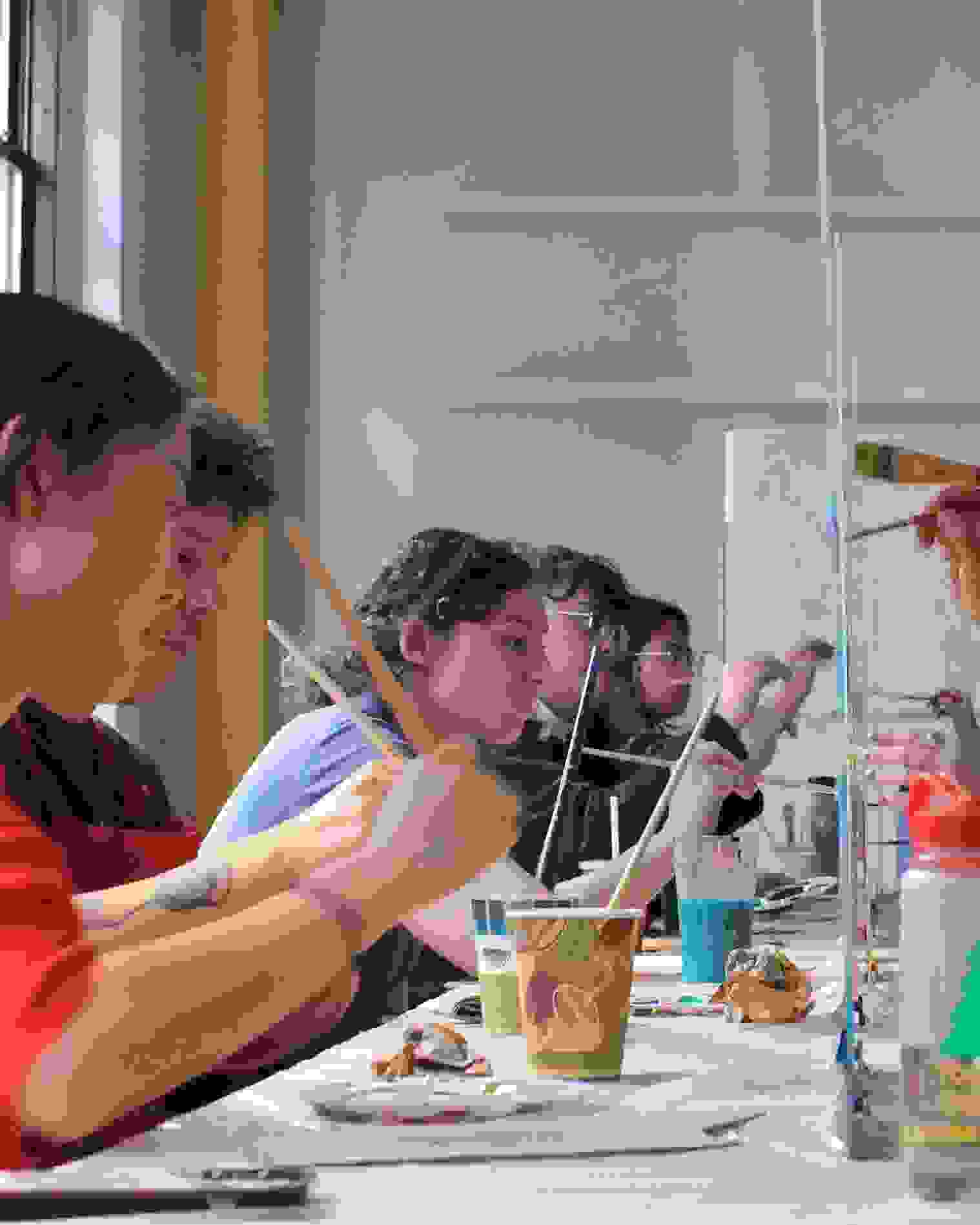 graduate students painting on either side of a plexiglass surface facing each other with paint and paintbrushes