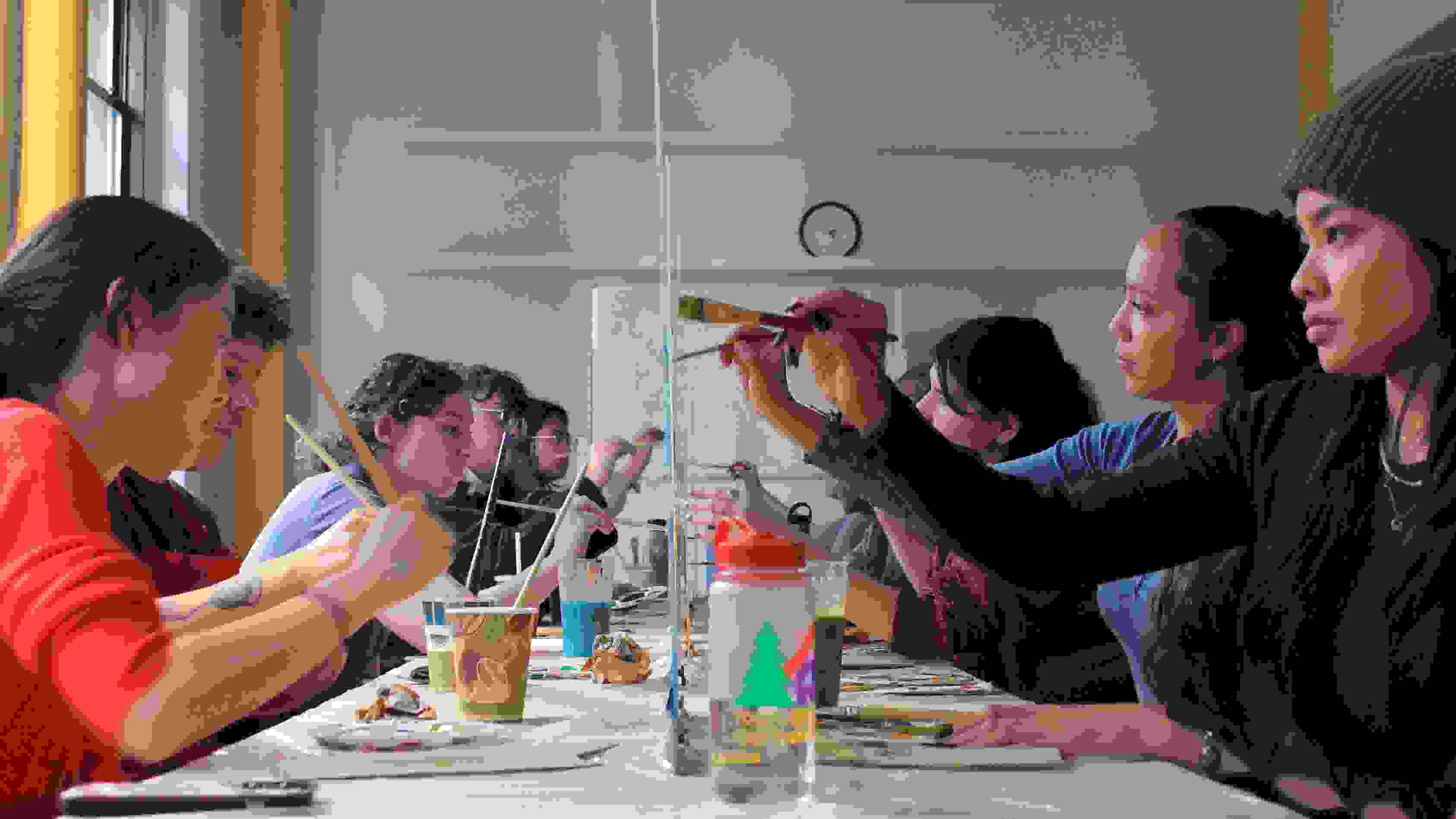 graduate students painting on either side of a plexiglass surface facing each other with paint and paintbrushes