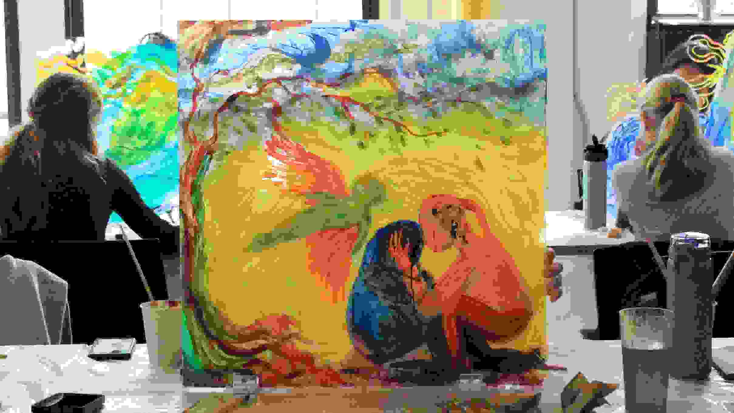 a square plexiglass painting of two figures embracing and an angel figure with tree; two students on the side of the painting with their backs turned away from camera