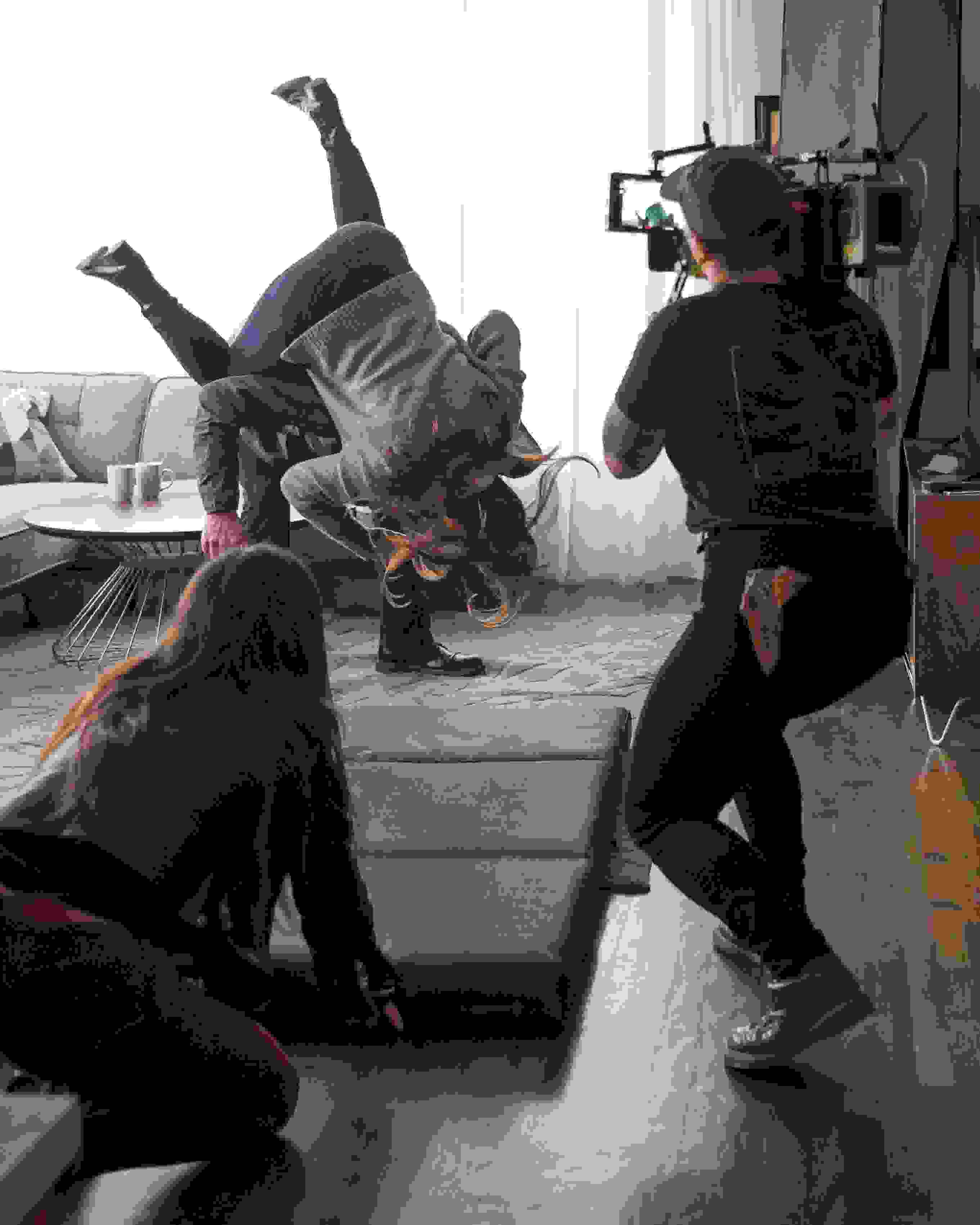 A camera person crouches to capture a fight scene taking place in front of a window.