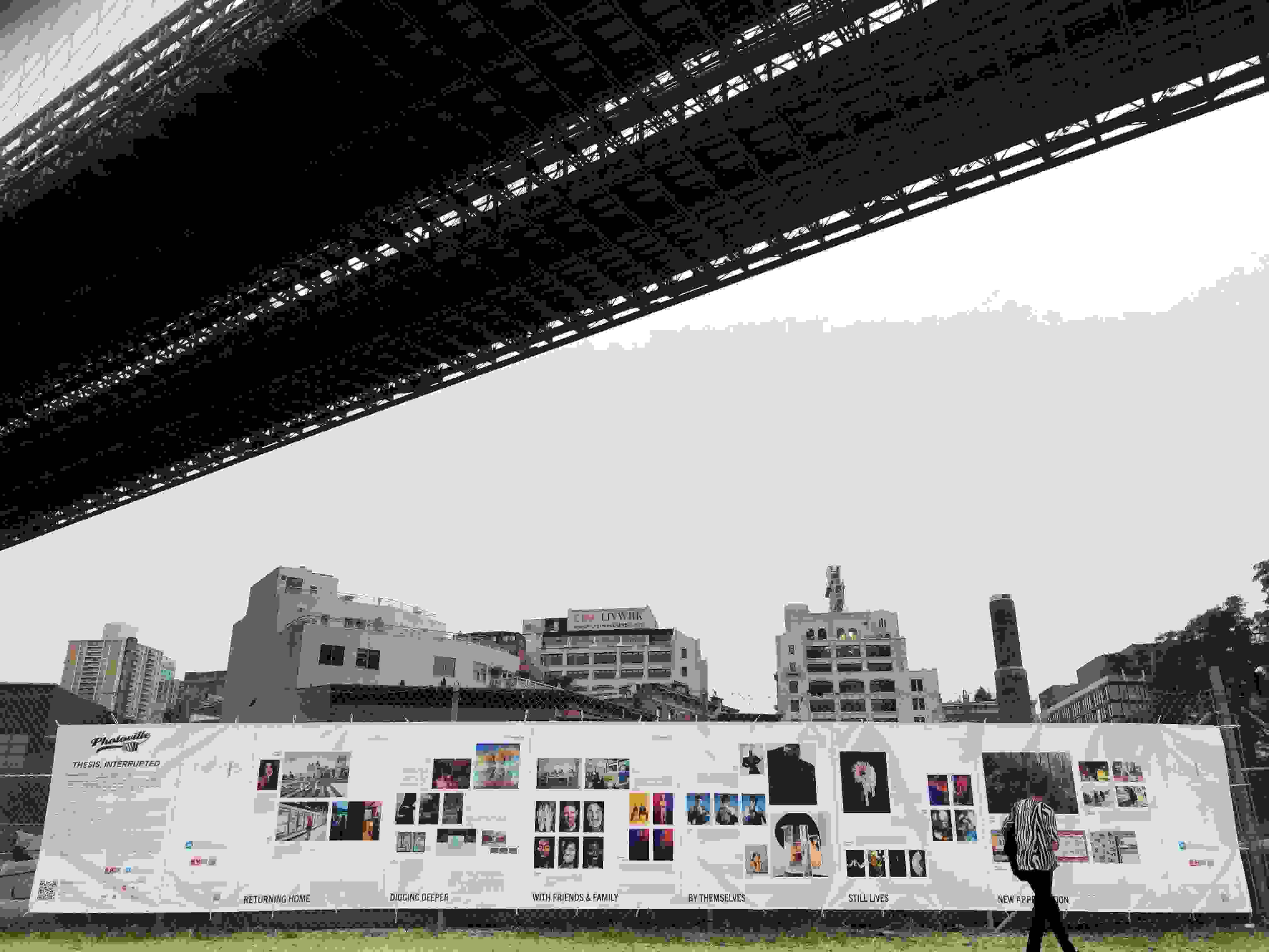 A very long white banner stretches across the lower half of the image, showing photographs by MPS Digital Photography graduates. Overhead is a bridge on an overcast day.