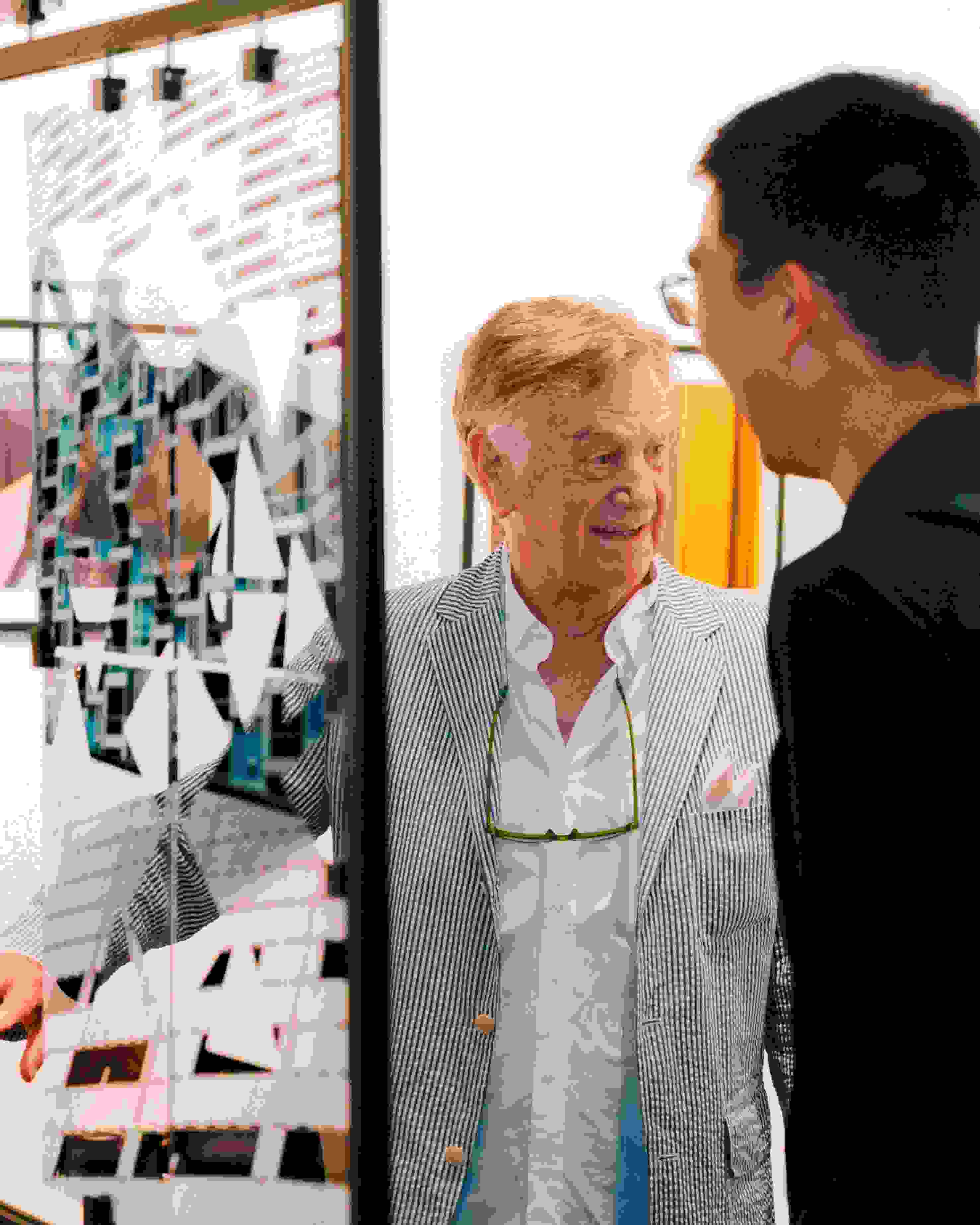 Person wearing a striped blue blazer standing in front of a piece of art talking with two other people.