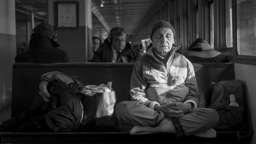 A black and white photo shows a man sitting with his legs crossed. The man's eyes are closed.