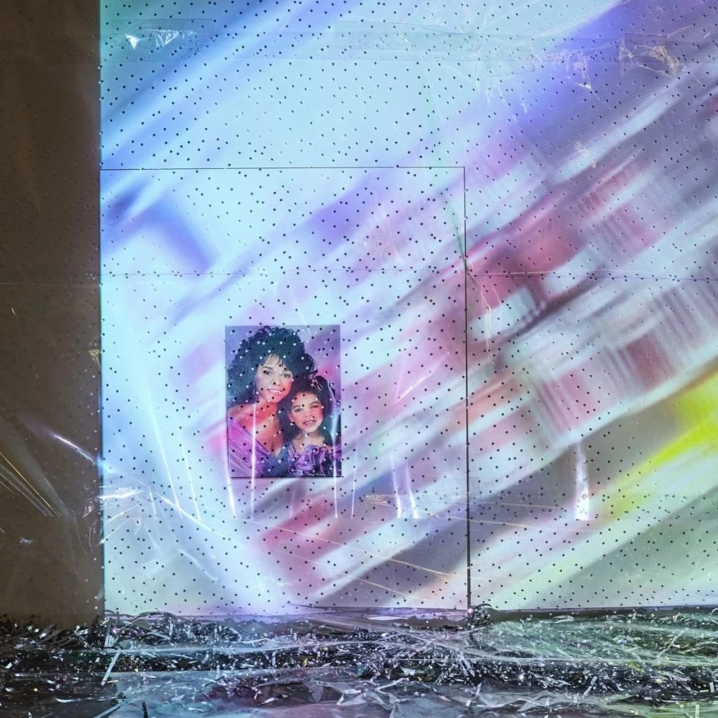 a painting of a woman and young girl in a white installation space, shrouded by cellophane and projected colorful images 