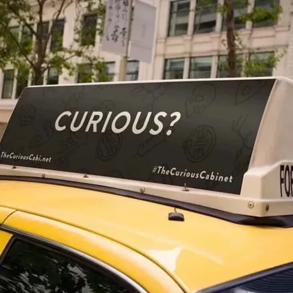 A closeup of a taxi top ad that says "Curious?" in white all caps text on a solid black background