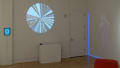 In a corner of the gallery, a circle divided into triangular sections is projected on one wall. A woman’s body is faintly projected catty-corner to it. To the left, an iPad is mounted on the wall.