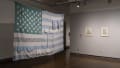 A large, light blue and turquoise colored American flag hangs from the ceiling. Two framed illustrations hang to the right.