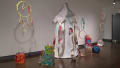 A wall with clown-themed sculptural pieces, including a tent and circus rings made of fabric and other soft materials.