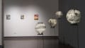 An image looking down the third gallery with paintings on the far wall, and paper lanterns on wire pedestals in front.