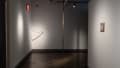 A corner of the gallery where a sculptural piece hangs from the ceiling to the floor, and another hangs diagonally across the wall.