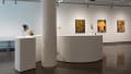 The first gallery with an S-shaped table depicting several sculptural pieces, with paintings on the wall behind.