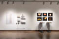 installation shot of unframed prints, tables with 3D objects, and shelves 