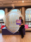 Student holding HBO logo sign in front of larger transparent Warner Brothers logo sign.