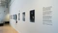 Angled view of the SVA Flatiron Windows hallway facing west; we see the title vinyl and a row of large black and white photographic prints.