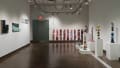 On the far wall in gallery two, narrow, vertical paintings that look like raw meat are hung in a row. On the left wall are the paintings that seem to be cut from a whole, and on the right are several pedestals displaying ceramic sculptures of objects stacked precariously high.