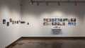 A view of the corner of the west and norths walls at the SVA Chelsea Gallery. Small paintings in blue and brown on panel hang on the left, and two rows of pinned illustrations are on the right under the title, “Voyages and Dreams.”