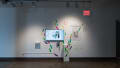 A monitor in gallery one is surrounded by colorful marks on the walls, which overflow onto the pedestal set in front of it. A poster beside the monitor reads “Outgrown.”