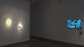In a corner of gallery one, spotlights are focused on a print and a hanging sculpture of a caterpillar. To the right, a monitor plays an animated video.