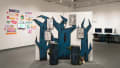 A divider in the middle of the room with cutouts of jagged, blue trees on top of it. Four frames of comics are on the trees, as well as an iPod and earphones. 