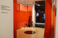 nstallation shot showing a black plexiglass organic shape hanging from the middle of the room surrounded by a red curtain and a black plexi circle immediately beneath it.