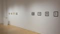 In the SVA Flatiron Gallery, several colorful prints are hung in a row on the left side of the wall. Several small black and white prints hang on the same wall towards the right.