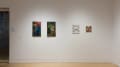 On another wall, two vertically-oriented paintings hang beside each other. They show tarot card-like characters. To their right, a black and white drawing and a small painting hang on the wall.