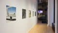 Inside the hallway, a row of photographs depict moments of daily life. The closest print shows the empty box of a trailer truck framing the landscape behind it.