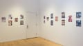 Colorful illustrative prints and comics hang in a patterned arrangement on the walls in the corner of SVA Flatiron Gallery.