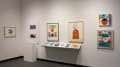  Many colorful collages of various sizes are displayed in a wall-mounted vitrine, on pedestals, and hung on the wall. Most of the works appear to be characters, like a koala wearing a hat and a funky-looking face with the word “WELL” above it.