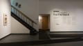 On a large wall beside a staircase, wall vinyl reads “Copy, Cut + Paste: The Visual Language of Ivan Chermayeff.” More text provides details and insight into the exhibition.
