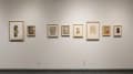Collages of varying sizes, using different materials and colors, hang in a row on a wall.
