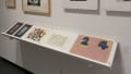 A shelf holds paper works which differ in content, but have overlapping similarities in style.