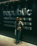 Student leans against large metallic Republic Records logo on wall.