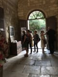 People gather at the entrance of the Romanesque cloister of Saint-Paul de Mausole. The floors and walls are made of stone, and natural light pours through the doorway.